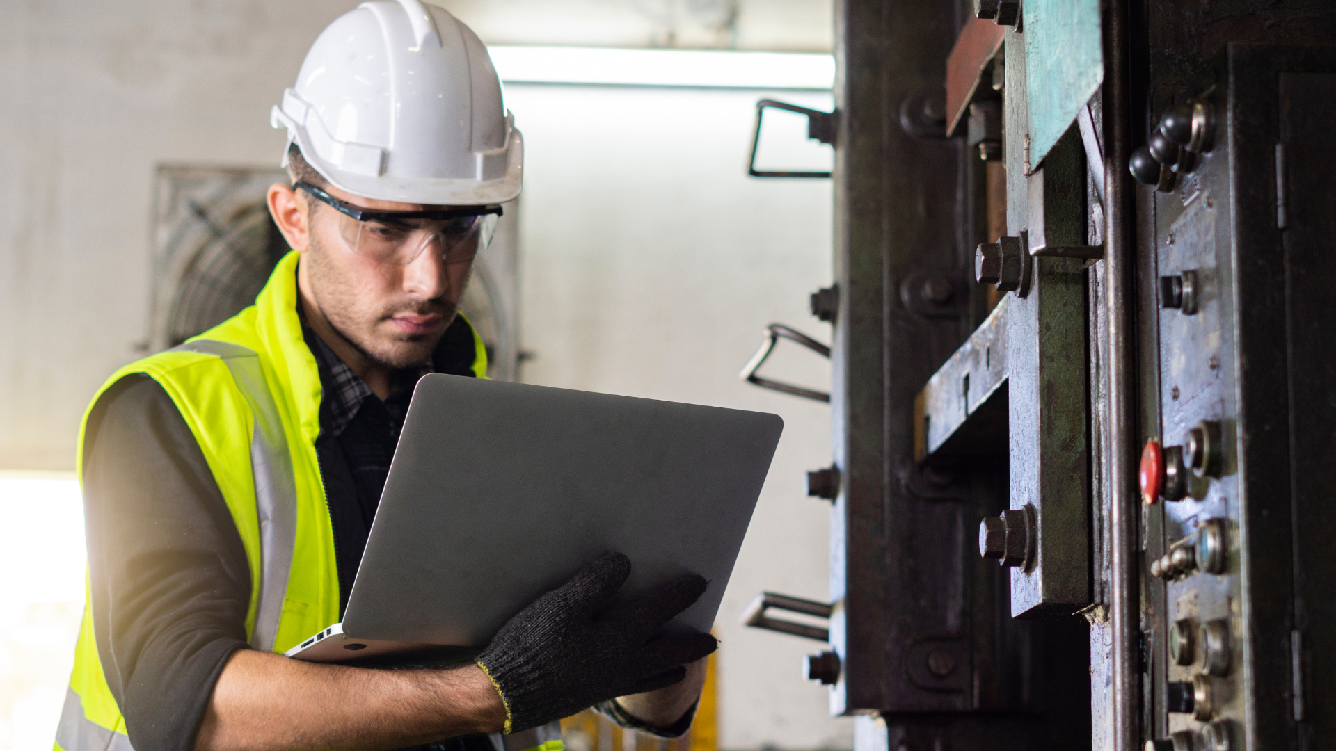 A man in a hard hat is looking at a tablet in front of a machine.