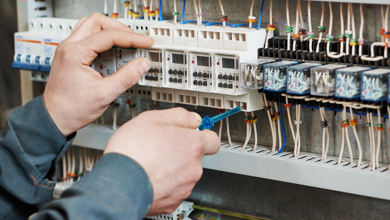 A man is working on an electrical panel with a screwdriver.