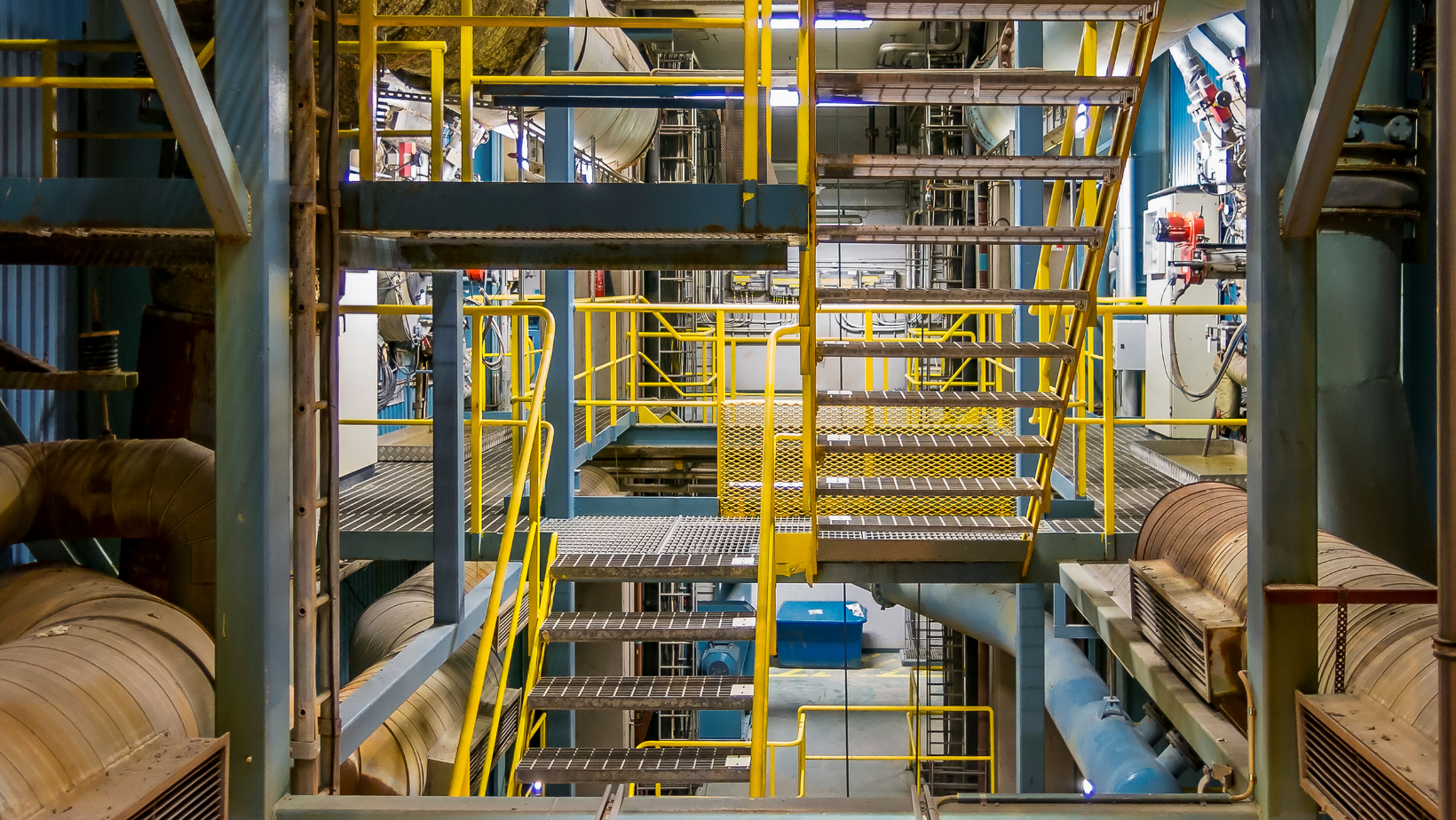 A factory with stairs and pipes and a yellow railing.
