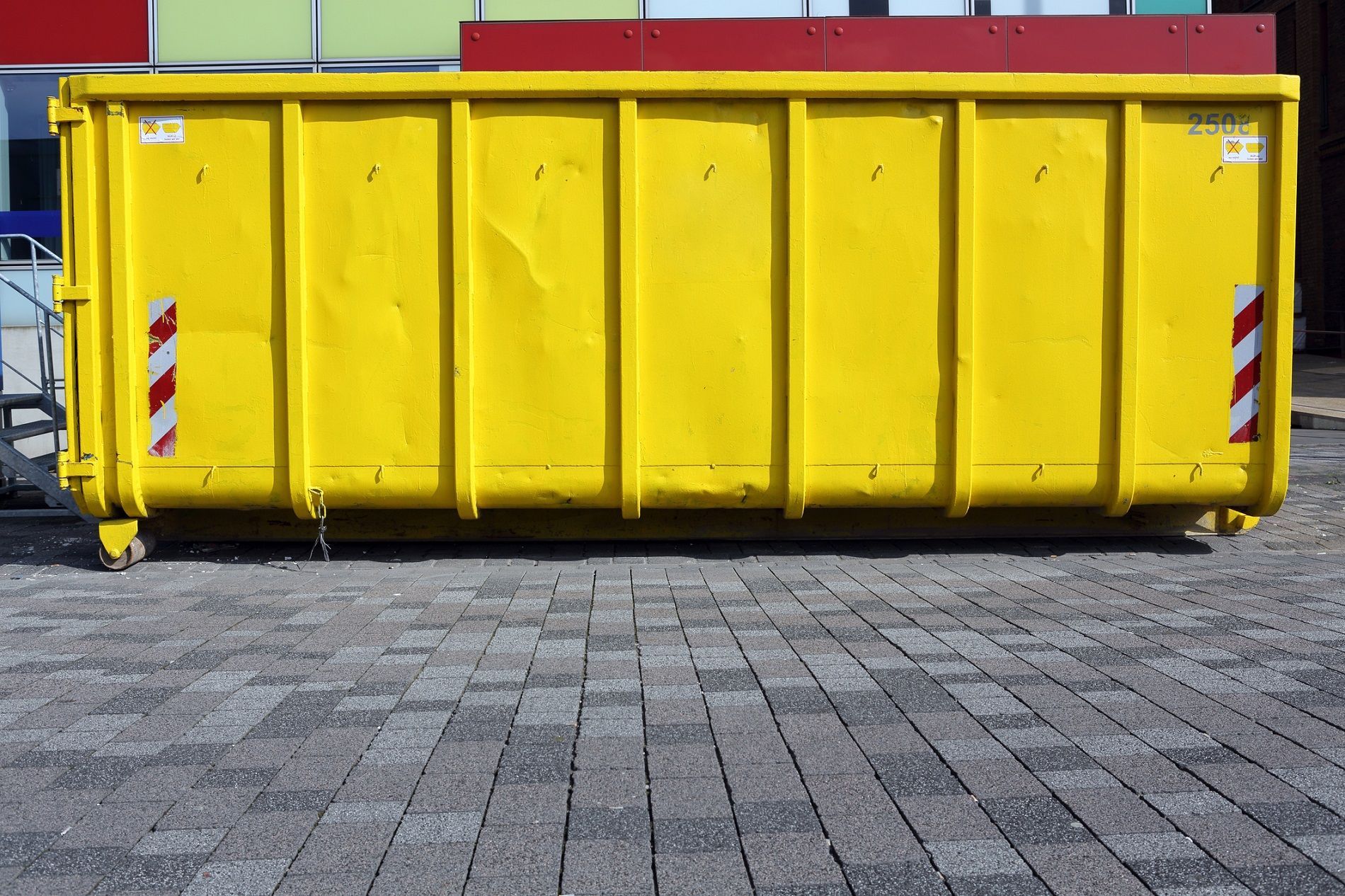 Image of a yellow industrial metal garbage container on a city street.