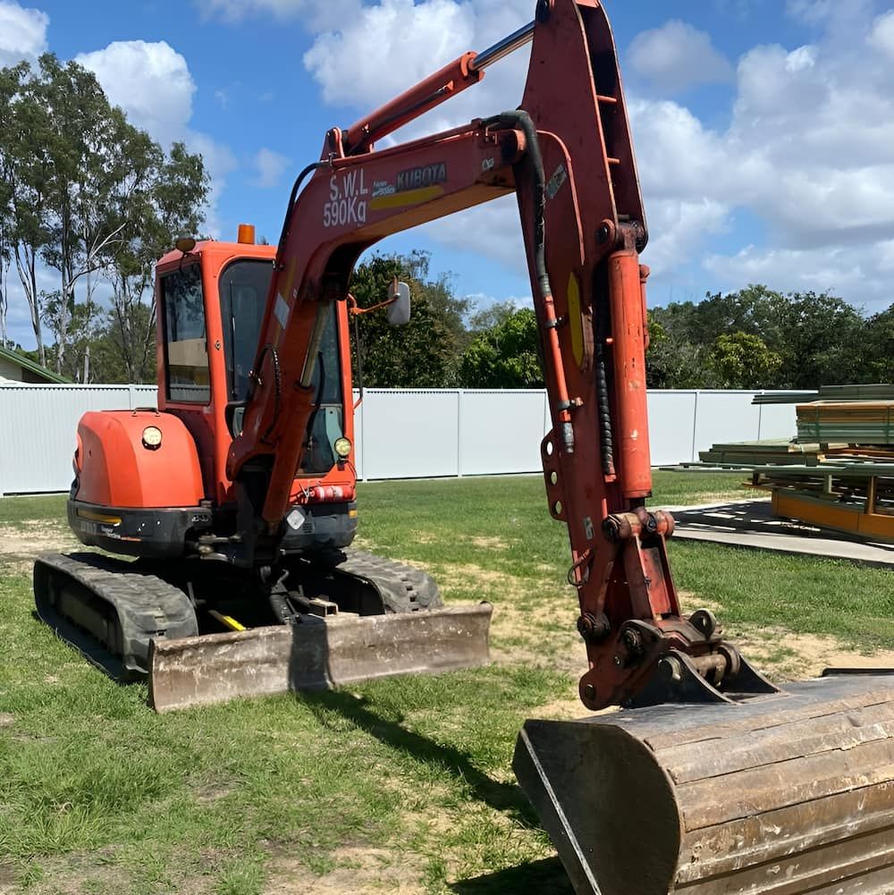 An Orange Excavator Is Parked In A Grassy Field — Josh's Diesel Services in Calliope, QLD