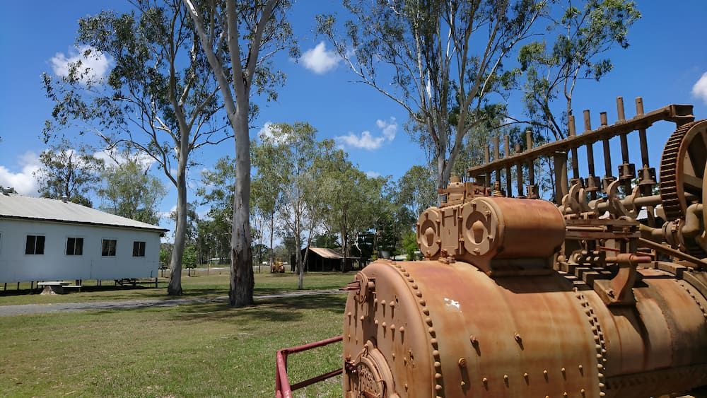 An Old Rusty Engine Is Sitting In A Grassy Field In Front Of A White Building — Josh's Diesel Services in Calliope, QLD
