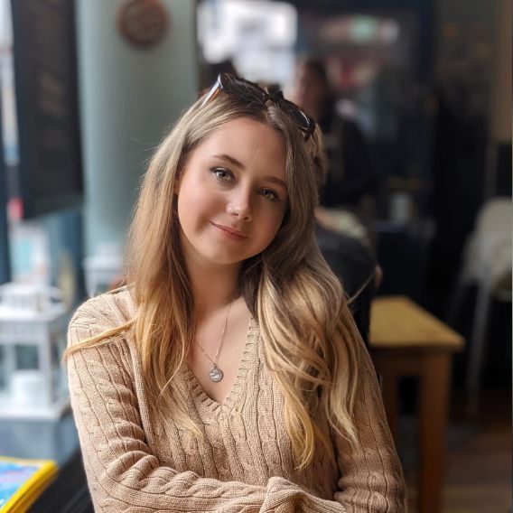 Image of Megan Conway with sunglasses on head smiling in a cafe, wearing a tan sweater.