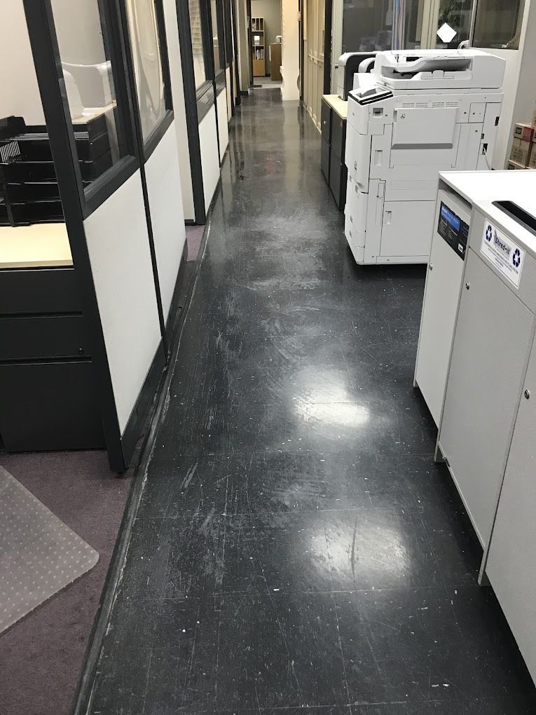 A long hallway in an office with a printer and cubicles.
