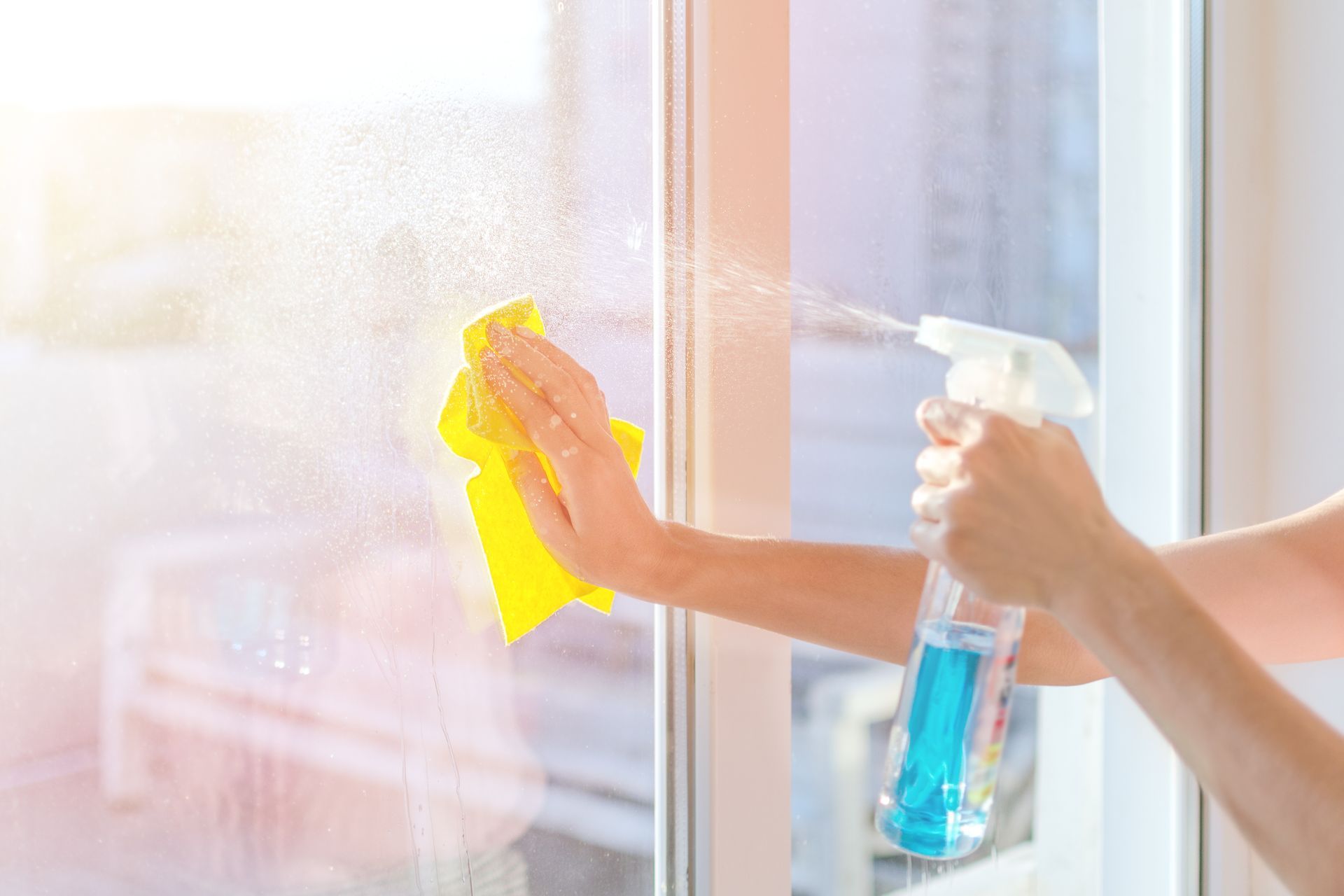 A woman is cleaning a window with a spray bottle and a yellow cloth.