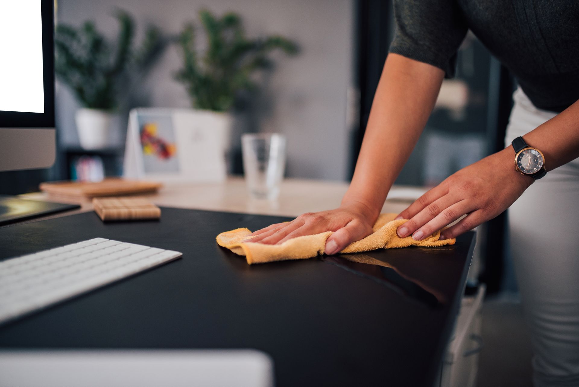 Person wiping a black desk with a yellow cloth in an office setting.