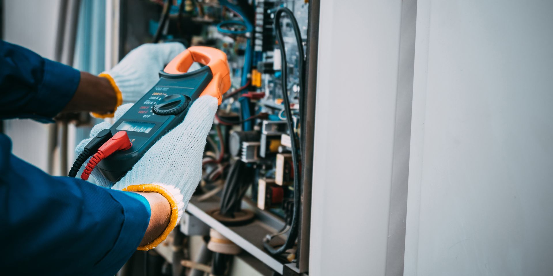 Un uomo sta usando una pinza amperometrica per testare una macchina.