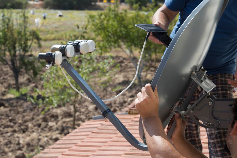 A Man Is Installing a Satellite Dish on A Roof — BTV Antenna & Data in Coral Cove, QLD