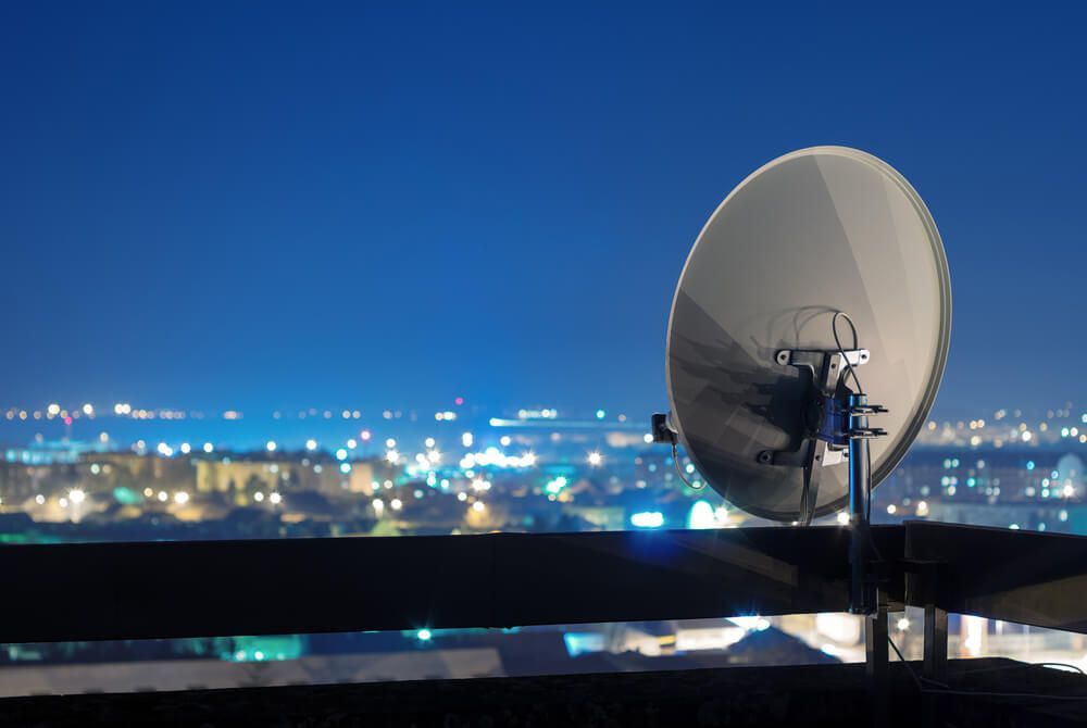 A Satellite Dish Is Sitting on Top of A Balcony Overlooking a City at Night — BTV Antenna & Data in Burnett Heads, QLD