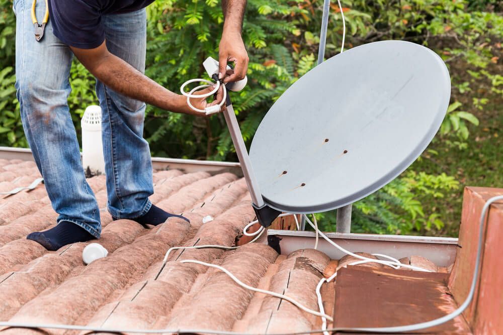 A Man Is Installing a Satellite Dish on The Roof of A House — BTV Antenna & Data in Bundaberg, QLD