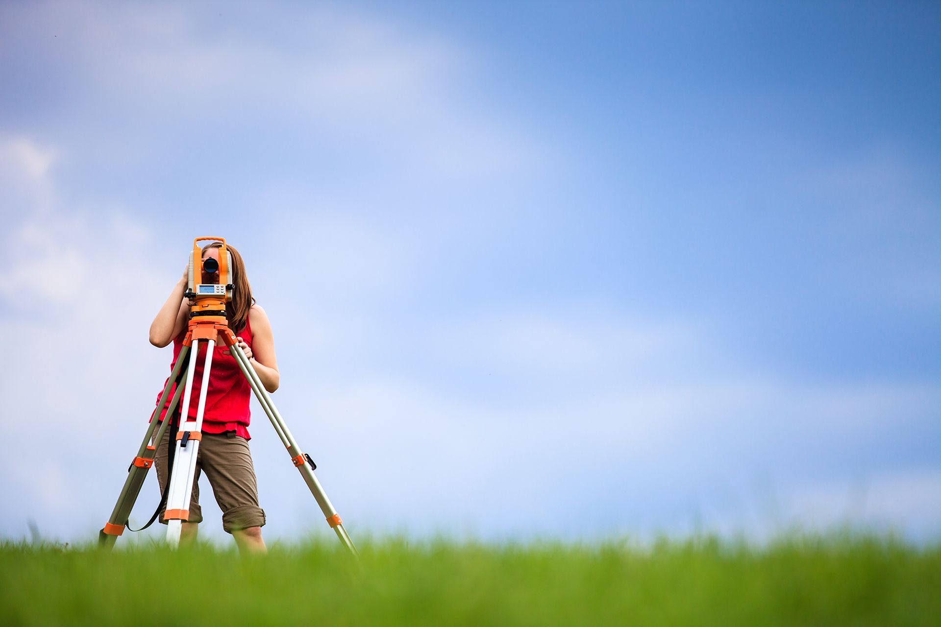 A woman is standing in a field looking through a telescope.