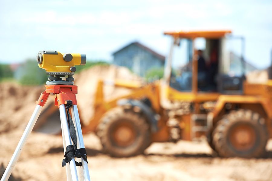 A level on a tripod with a bulldozer in the background.