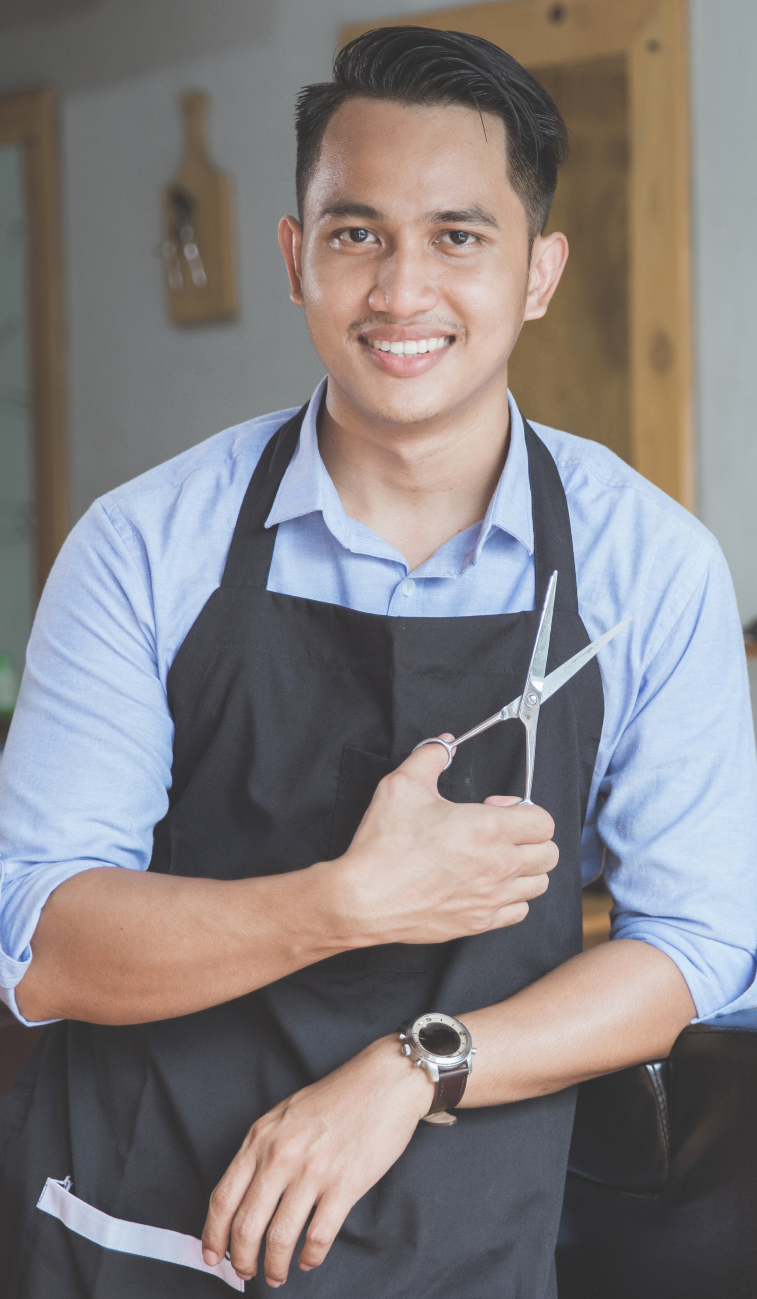 a man in an apron is holding a pair of scissors .