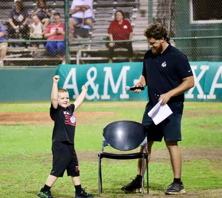 A man and a boy on a baseball field with a sign that says a & m