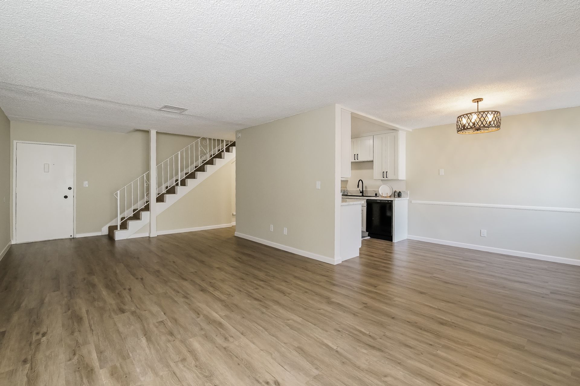 An empty living room with hardwood floors and stairs leading to the kitchen.