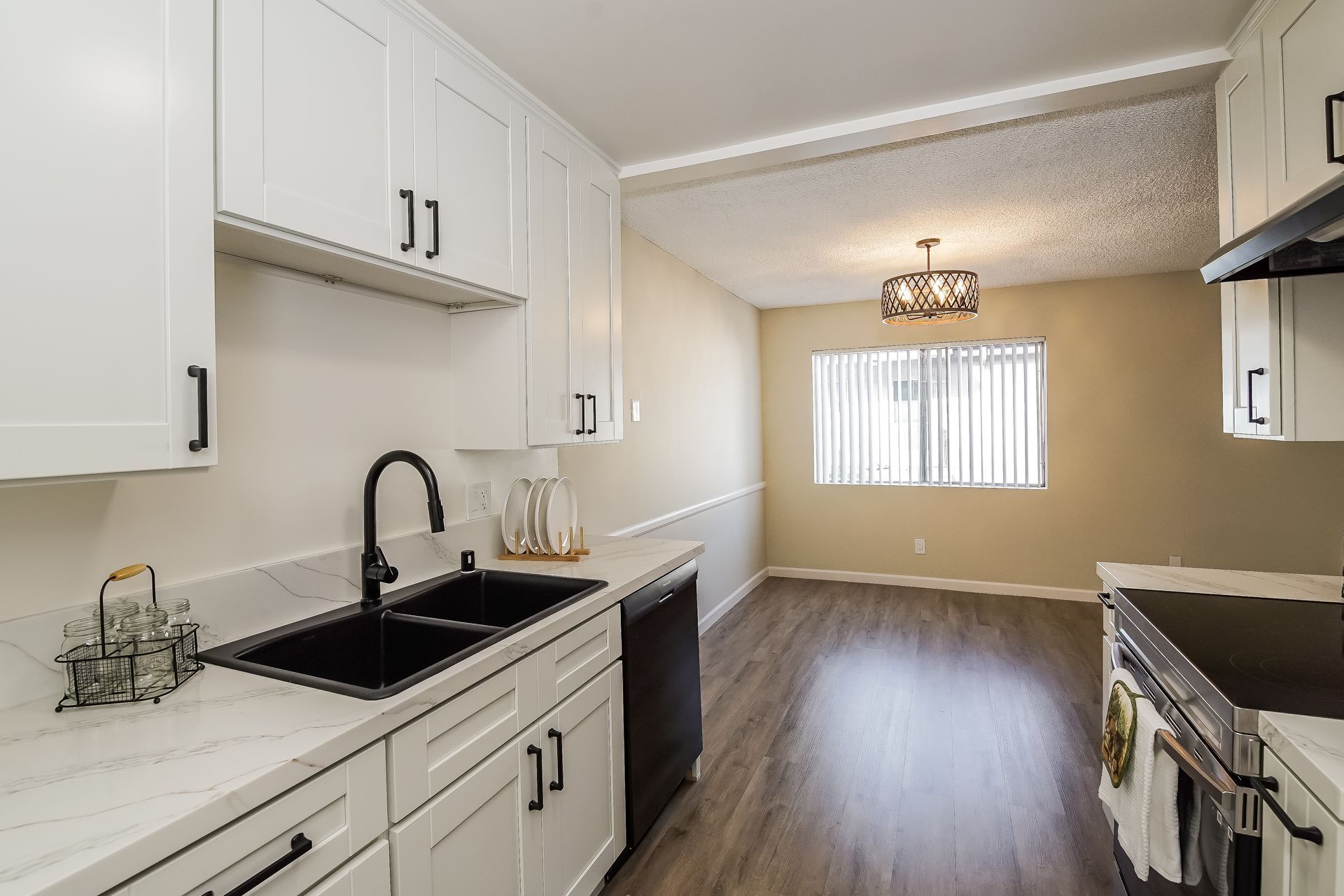 A kitchen with white cabinets , a sink , a stove , and a window.