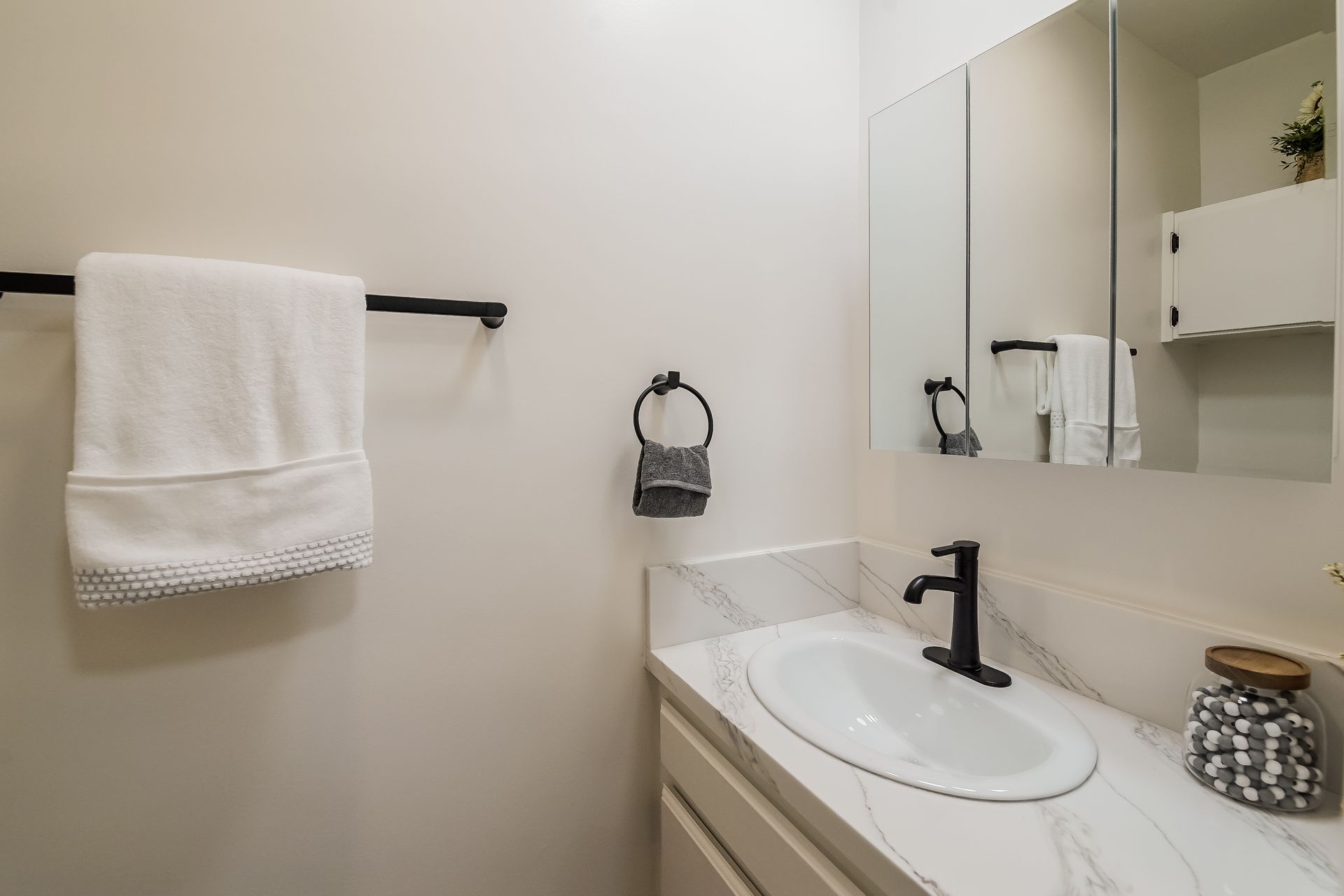 A bathroom with a sink, mirror and towel rack.