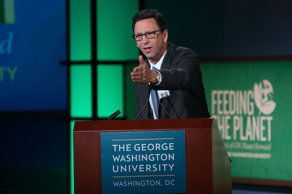 a man is giving a speech at the george washington university Feeding the Planet Conference