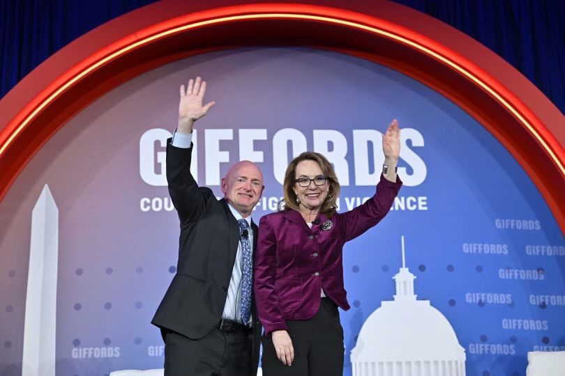 Gabby Gifford and her husband waving in front of the Giffords Law Center logo at the annual conference