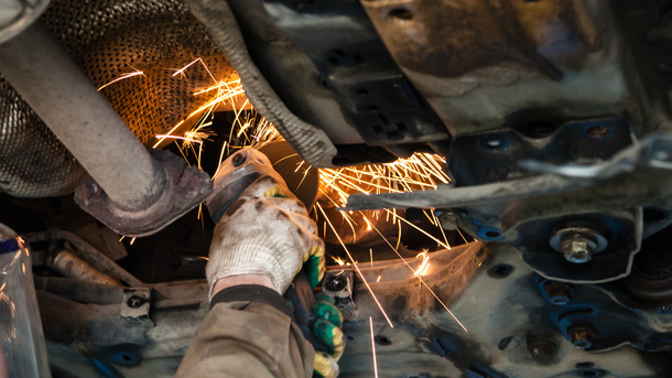 Mechanic using a grinder, creating sparks beneath a car.