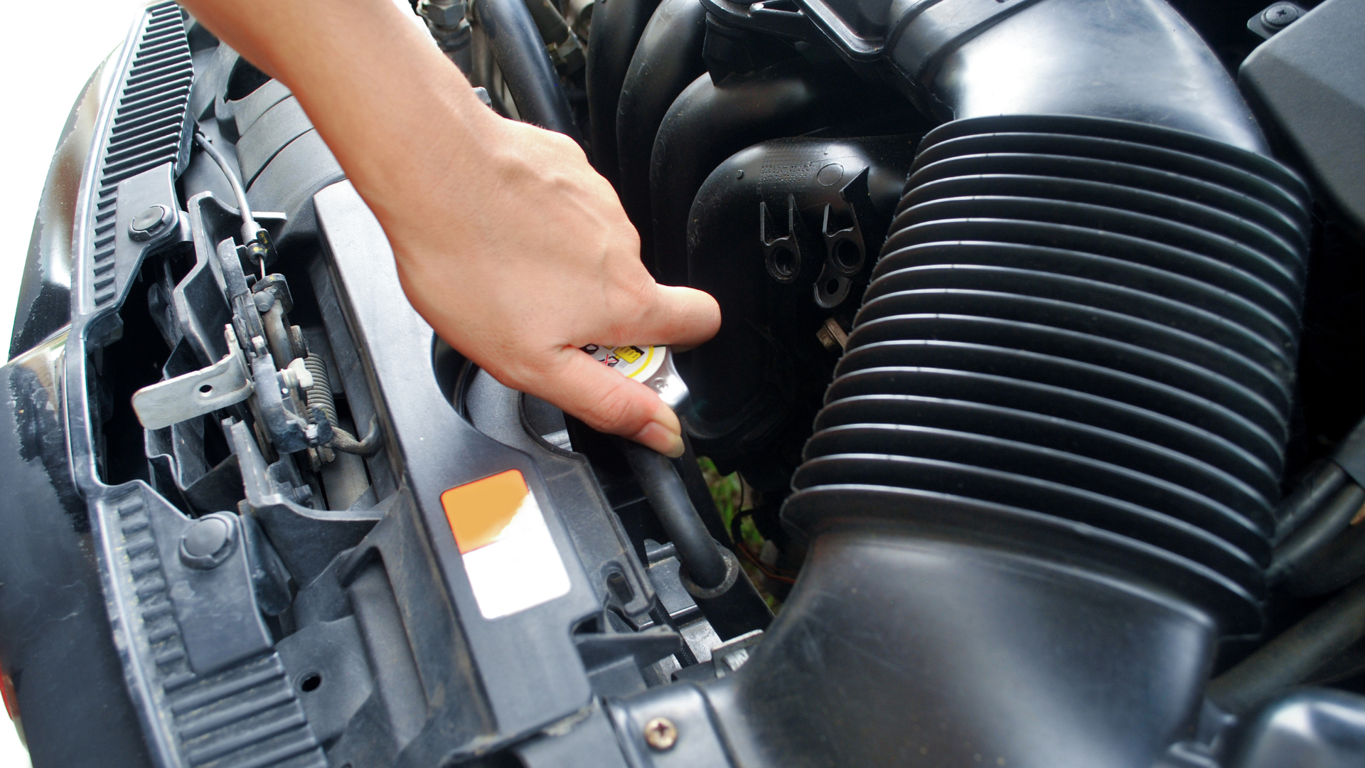 Hand reaching to open a car's radiator cap in the engine compartment.