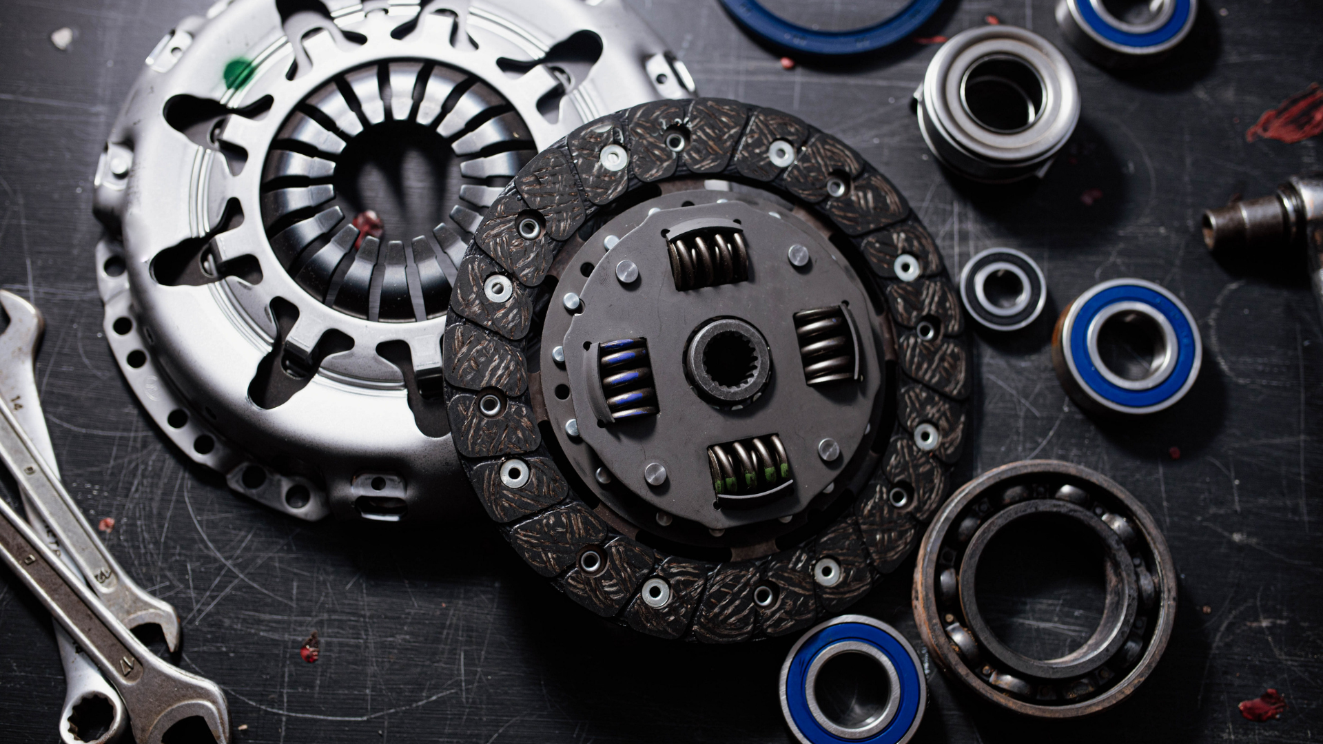 Clutch and other car parts, including bearings and wrenches, arranged on a dark surface.