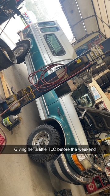 A van in a garage, being worked on. The van is teal and silver. The mechanic is providing maintenance before the weekend.