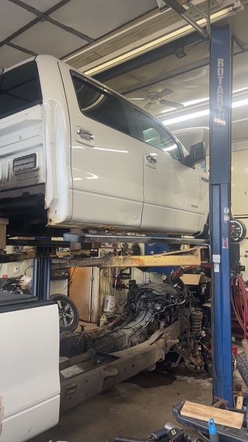 White truck cab lifted on a hoist in a garage, chassis below.