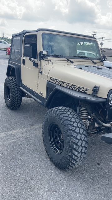 Tan Jeep Wrangler with black fenders, large tires, and the words 