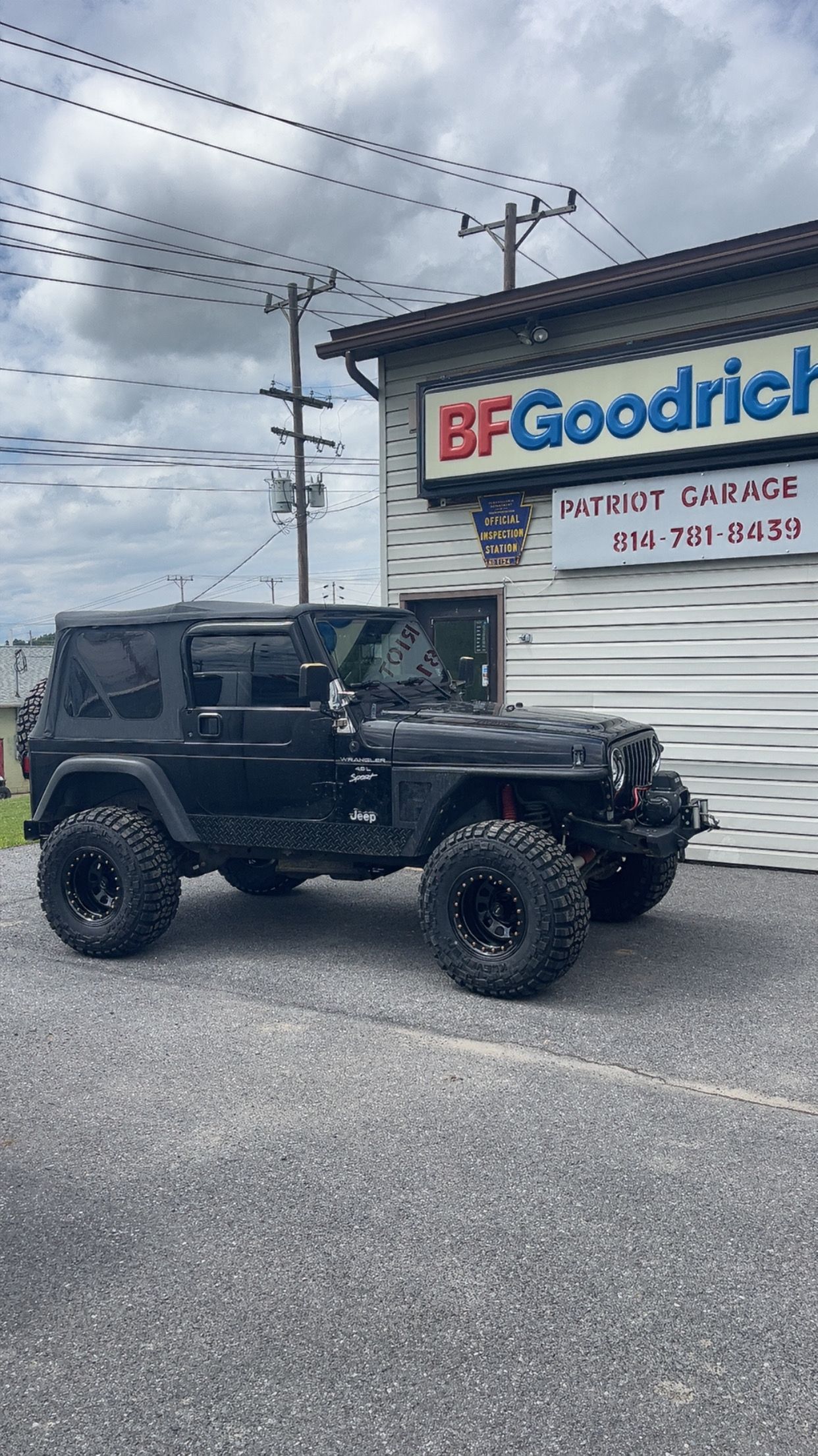 Black Jeep Wrangler with large tires parked outside a BFGoodrich garage.
