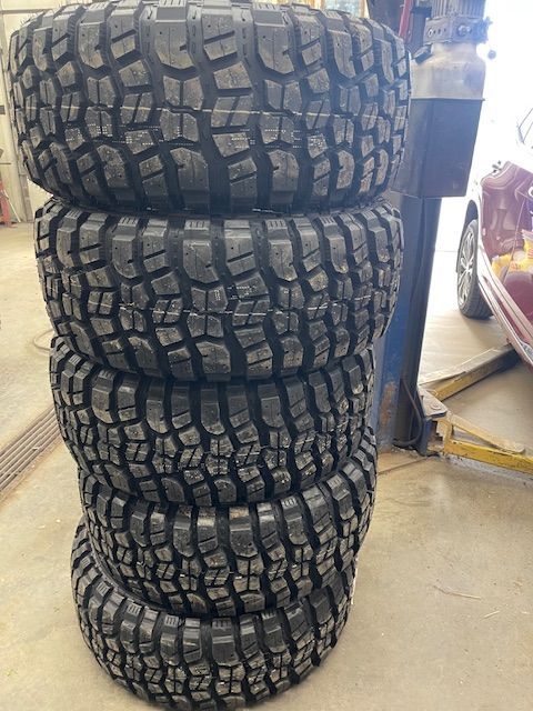 Five off-road tires stacked on top of each other, in a garage setting.