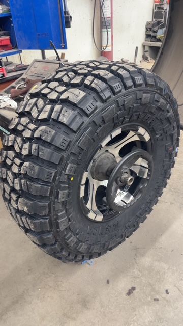 Large black off-road tire mounted on a silver and black wheel, in a garage.