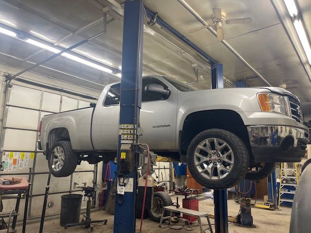 Silver pickup truck elevated on a car lift in a repair shop.