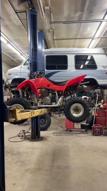 Red ATV lifted on a car lift in a garage, a van in the background.