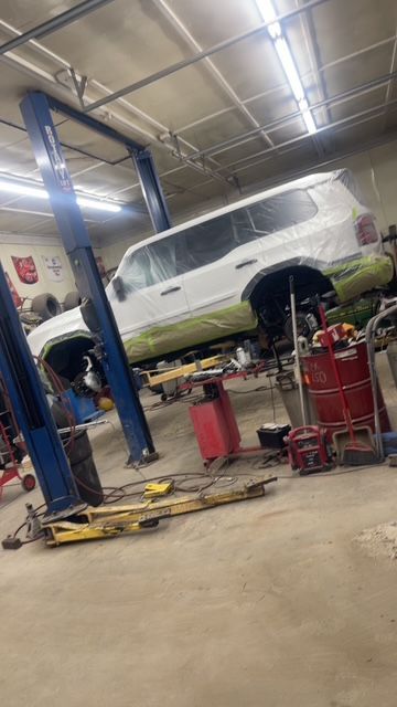 White SUV on a lift in a garage; mechanic working below.