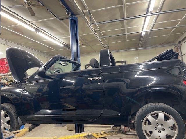 Black Chrysler PT Cruiser convertible on a lift, hood up, in a garage setting.