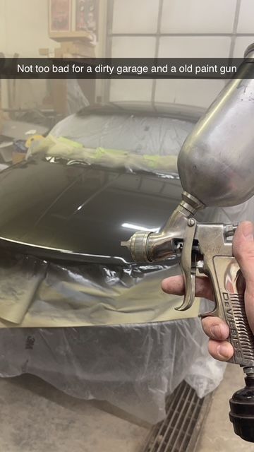 Person spraying paint on a car with an old paint gun in a garage.