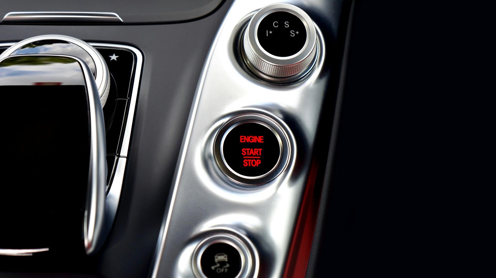 Car dashboard with start/stop button, silver panel, and black screen.