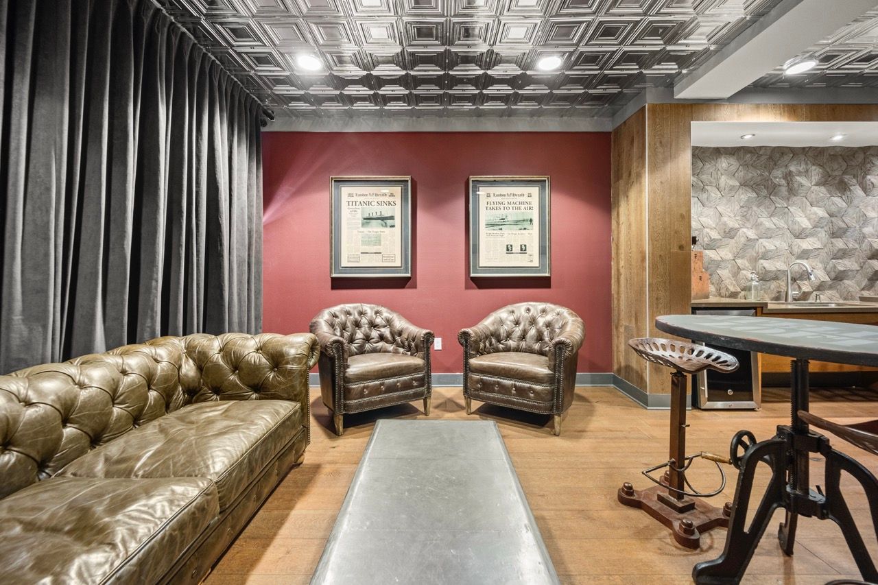 Community lounge with tufted brown leather seating, framed posters on a red wall, and a bar-height table.