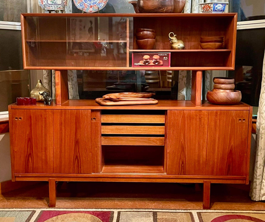 A mid-century modern teak wood hutch with open shelving, glass sliding doors, cabinets, and drawers.