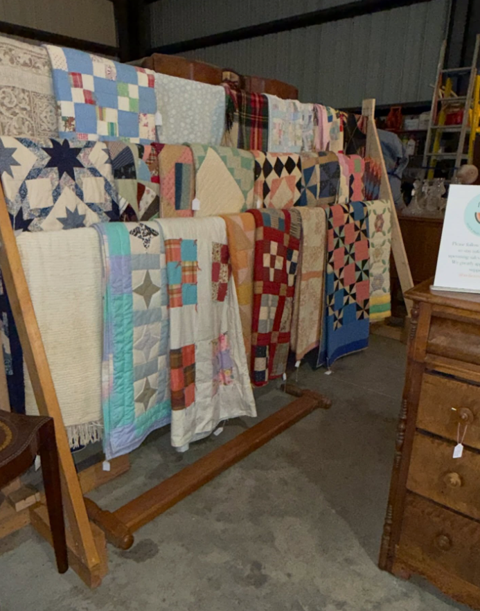 A wooden display rack holds a variety of colorful patterned quilts in a shop.