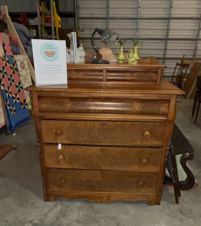 A wooden three-drawer dresser with a small hutch, topped with decorative vases and a lamp in an indoor setting.