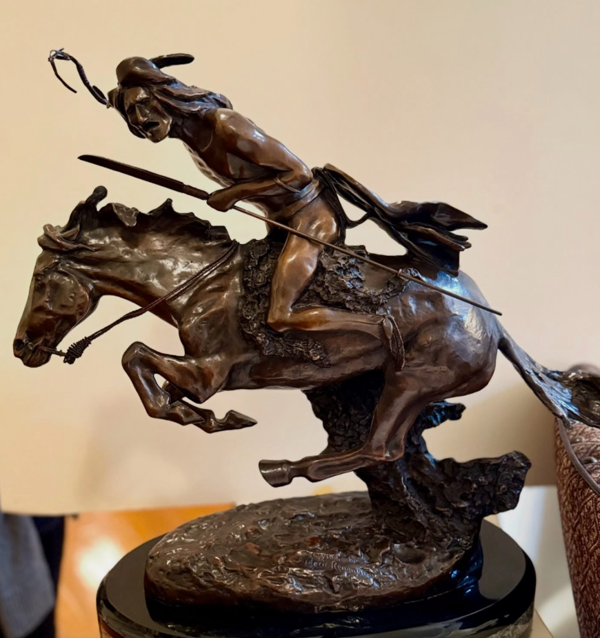 A bronze sculpture of a figure riding a leaping horse, holding a spear and wearing a headdress on a dark base.