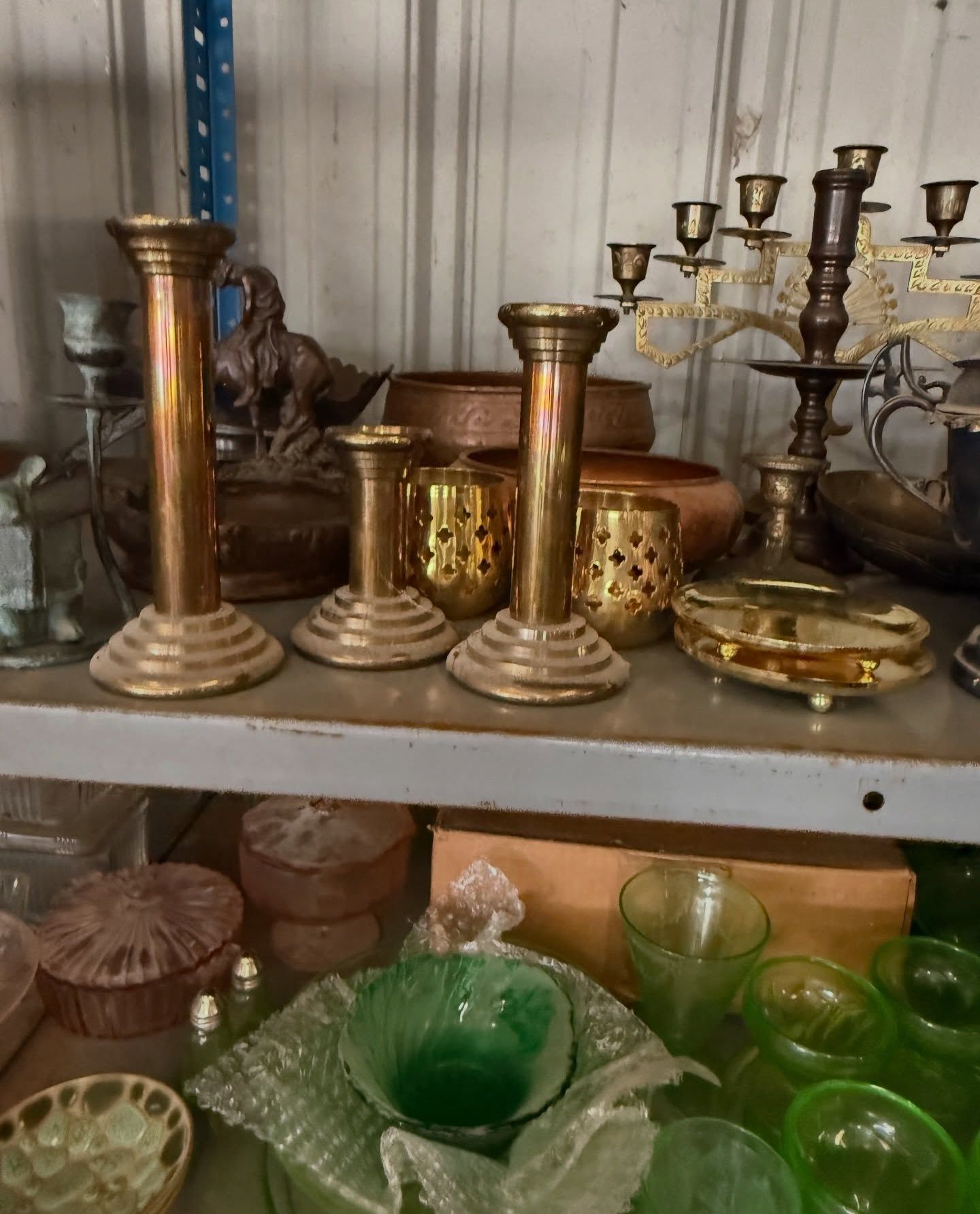 A shelf filled with assorted antique brass candlesticks, a candelabra, and green glassware items.