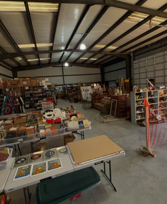 A wide-angle view of a large warehouse space filled with tables, shelves, and boxes of vintage items and collectibles.