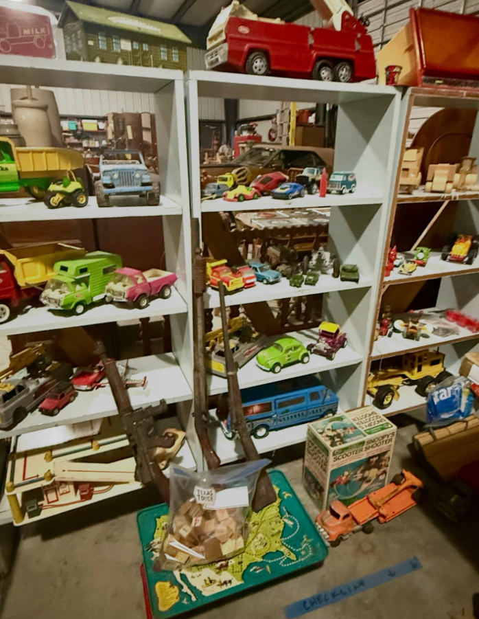 Shelves filled with various vintage toy vehicles, including trucks, cars, and a red fire truck, in a storage area.
