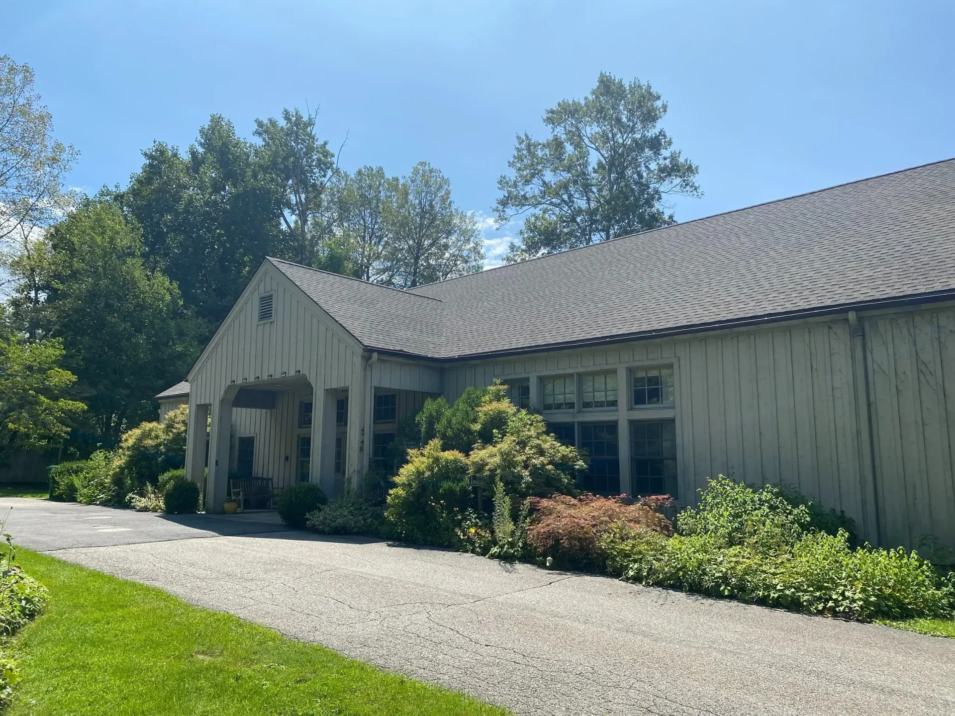 A light-colored building with a gravel driveway, surrounded by greenery under a blue sky.