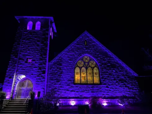 Church at night illuminated in purple lights, stained glass window glows yellow.alk Performing 