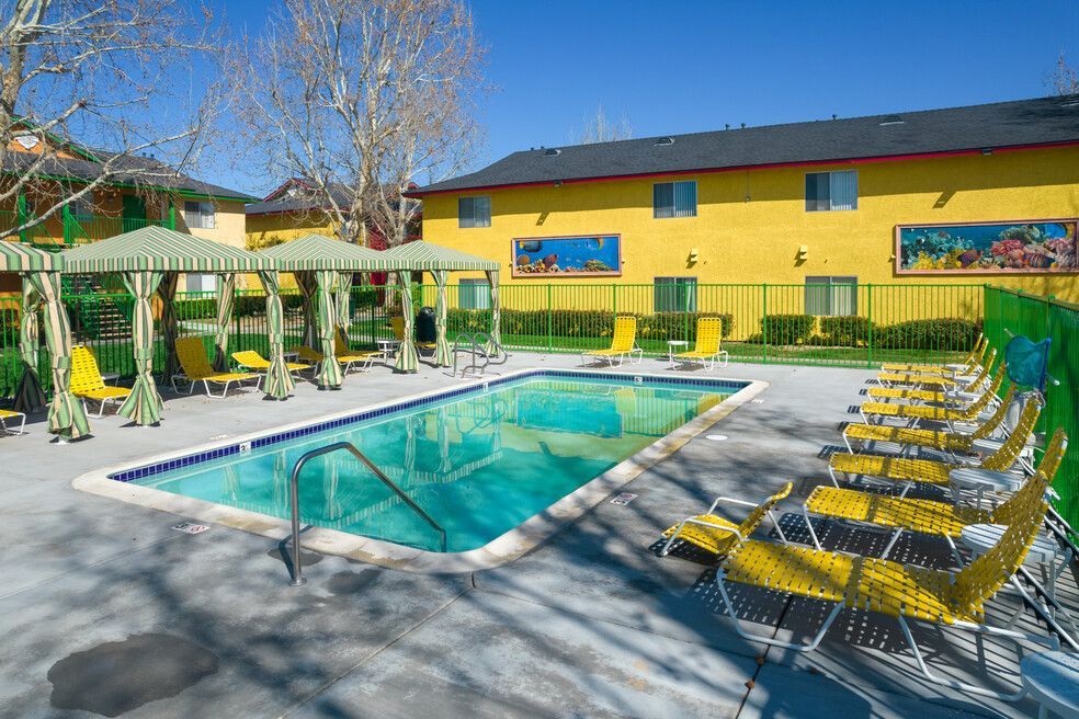 A large swimming pool surrounded by chairs and umbrellas in front of a yellow building.
