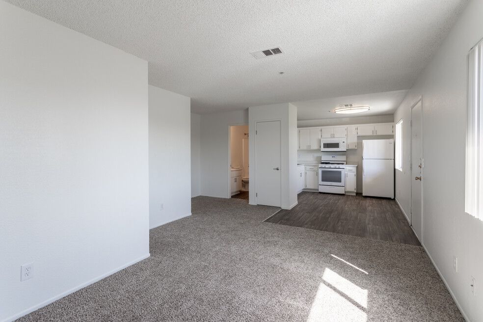 An empty living room with a kitchen in the background.